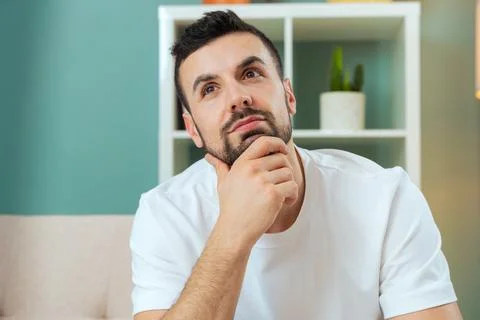 Thoughtful young man facing the camera while leaning forward on the sofa Stock Photos