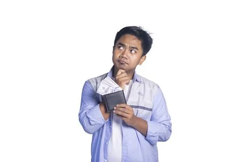 A thoughtful young man looking up while holding a black wallet filled with .. Stock Photos