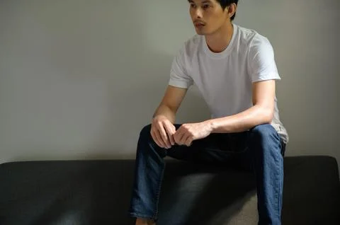 Thoughtful Young Man in Plain T-Shirt Sitting on Sofa Stock Photos