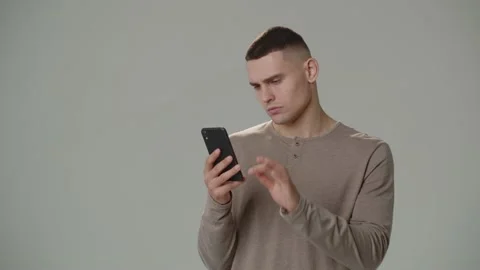 Thoughtful young man scrolling through the news feed on his smartphone. Studio Stock Footage 234897663