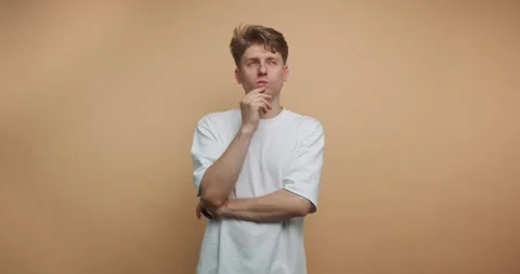 Thoughtful young man in a simple white shirt poses against a neutral backdr.. Stock Footage 317328056