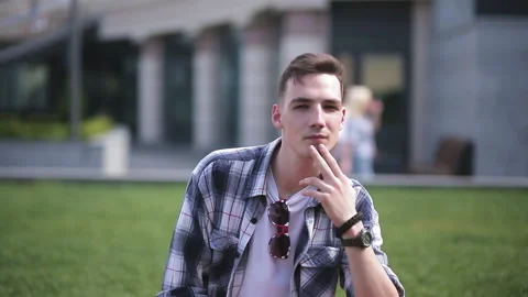 Thoughtful young man sitting on the grass downtown waiting for his friends or Stock Footage 131777600