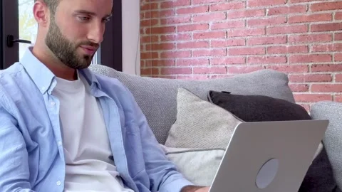Thoughtful young man working on a laptop computer while sitting Stock Footage 345077955