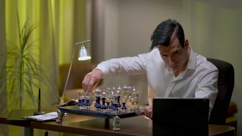 Thoughtful young Middle Eastern man playing chess at home checking online video Stock Footage 153700755
