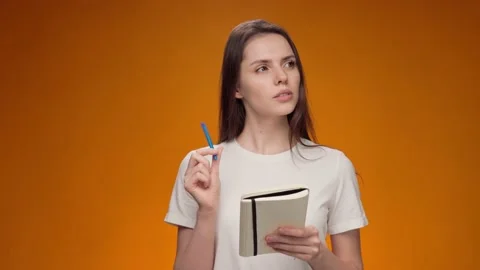 Thoughtful young woman making notes in notepad against yellow background Stock Footage 148829853