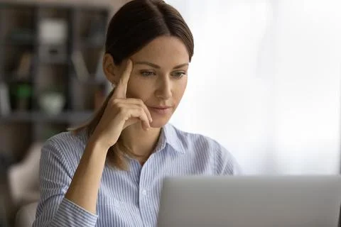 Thoughtful young woman read document on computer screen at workplace Stock Photos