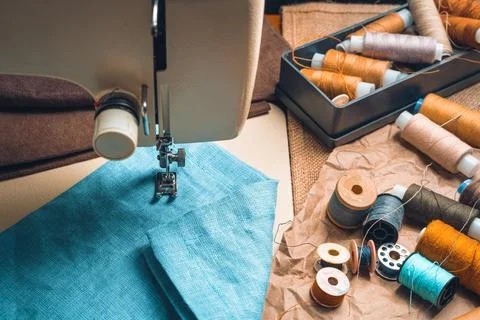 Thread, scissors, and fabric against a blurry sewing machine. Stock Photos