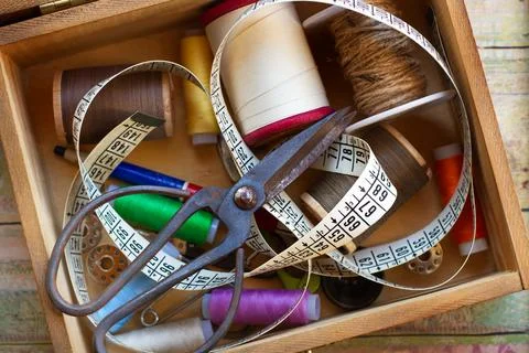 Thread, scissors and a measuring tape in a wooden box on a wooden table Foto stock