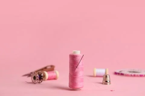Thread spool and thimble on pink background, closeup Stock Photos
