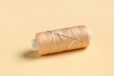 Thread spool with needle on beige background, closeup Stock Photos