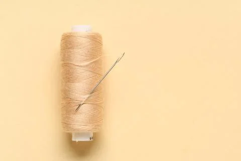 Thread spool with needle on beige background, closeup Stock Photos
