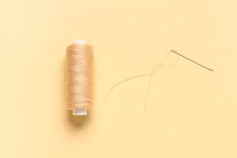 Thread spool with needle on beige background, closeup Stock Photos