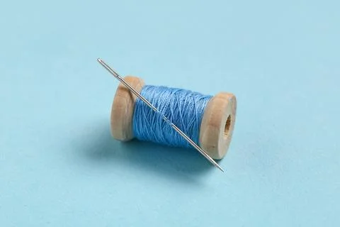 Thread spool with needle on blue background, closeup Stock Photos