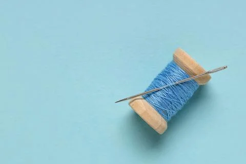 Thread spool with needle on blue background, closeup Stock Photos