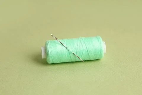 Thread spool with needle on green background, closeup Stock Photos