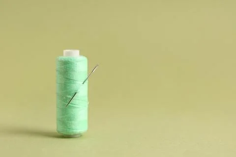 Thread spool with needle on green background, closeup Stock Photos