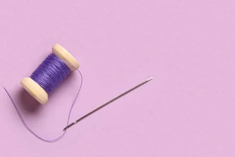 Thread spool with needle on lilac background, closeup Stock Photos