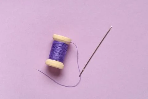 Thread spool with needle on lilac background Stock Photos