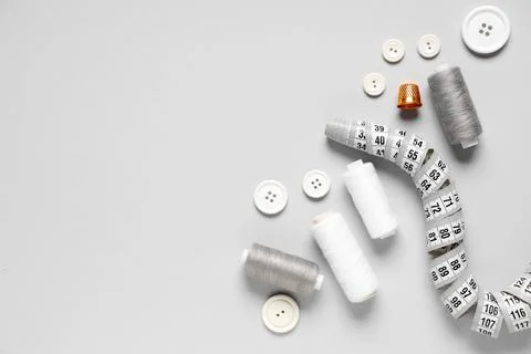 Thread spools with buttons, measuring tape and thimble on grey background 写真素材