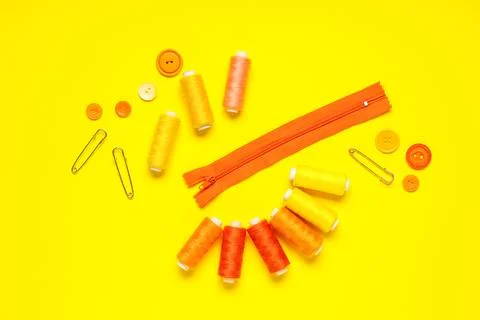 Thread spools with buttons, zipper and pins on yellow background 写真素材
