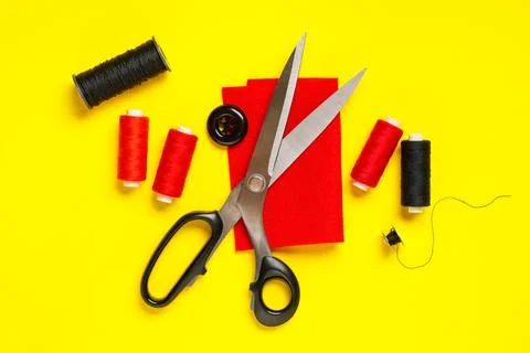 Thread spools with scissors, cloth and button on yellow background Stock Photos