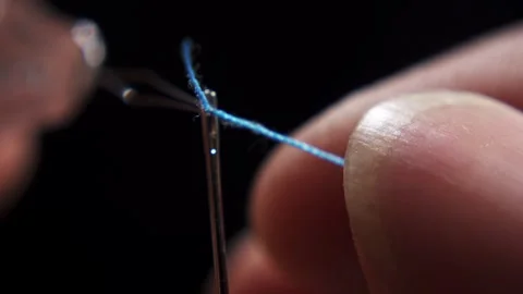 A thread that is threaded through the eye of a needle on black background Stock Footage 287228457