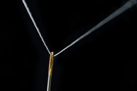 Thread threaded through the eye of a needle in close-up on a black background Stock Photos