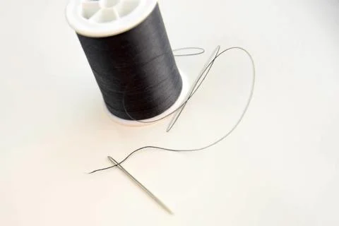 Threaded needle and black spool of thread Stock Photos