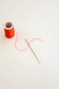 Threaded needle and red spool of thread Stock Photos