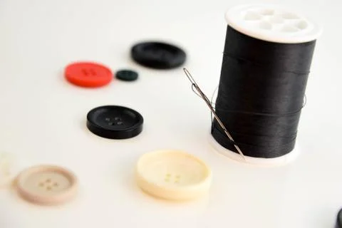 Threaded needle, black thread spool and buttons Stock Photos