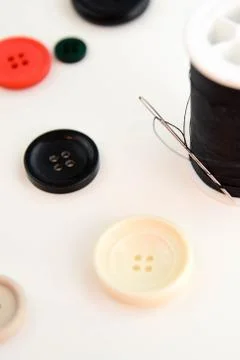 Threaded needle, black thread spool and buttons Stock Photos