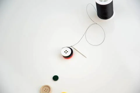 Threaded needle, buttons, and black spool of thread Stock Photos