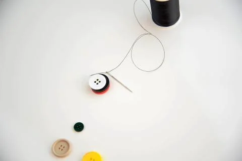 Threaded needle, buttons, and black spool of thread Stock Photos