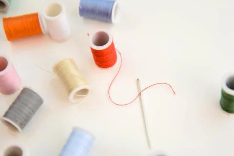 Threaded needle, red thread spool, and multi colored spools Stock Photos