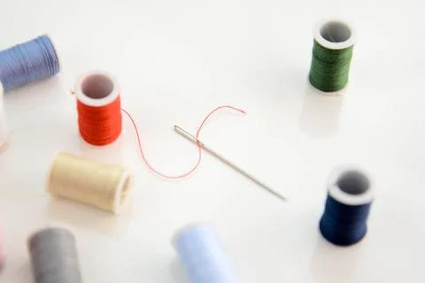 Threaded needle, red thread spool, and multi colored spools Stock Photos