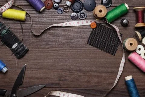 Threads buttons and needles over brown wooden table Stock Photos