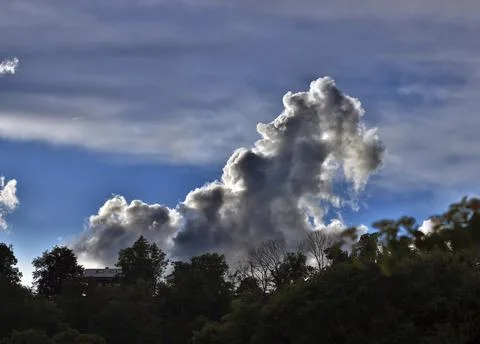 Threatening thundercloud grows behind a house into the blue sky, dramatic cloud Stock Photos