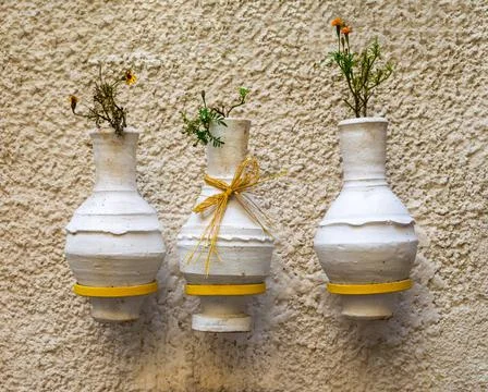 Three adjacent handmade white pottery vases, hanged on rough stone white wall Stock Photos