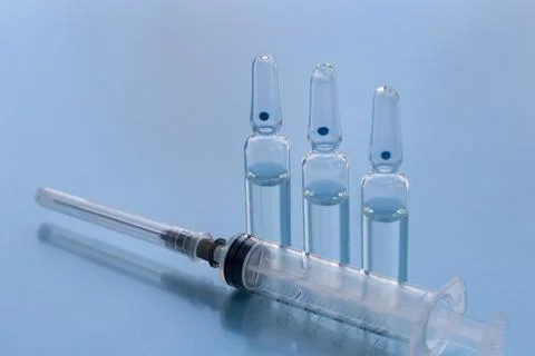 Three ampullas and expendable syringe isolated on blue background. Stock Photos
