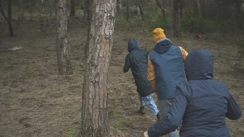 Three anonymous people run through the trees of a pine forest disappearing behin Stock Footage 106958194