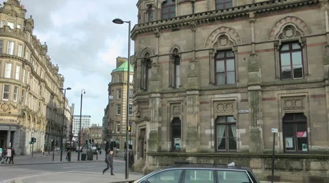Three anonymous people, with suitcase on wheels, one points up at  building Stock-Footage 1080021