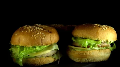 Three appetizing burgers revolve on a black background Stock Footage 84231365