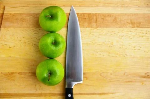 Three apples on a cutting board, with sharp knife Stock Photos