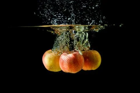 Three apples splashing into water on black background. Stock Photos