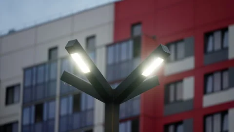 Three-armed LED streetlight glowing at dusk in front of a modern residential Stock Footage 317575037