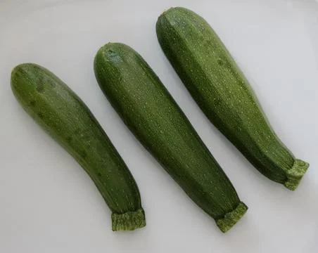 Three assorted green courgettes lying on a plain white background Stock Photos