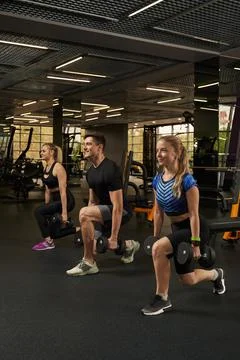 Three athletic young men squat with dumbbells in the gym Stock Photos