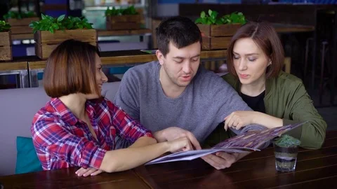 Three attractive young people in a cafe or restaurant choose a menu of drinks Stock Footage