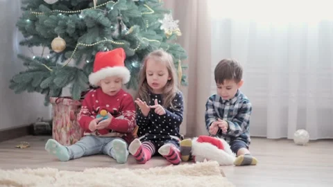 Three authentic happy Joy children count fingers sit by Christmas tree playing Stock Footage 152878734