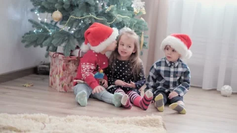 Three authentic happy Joy children sit by decorated Christmas tree playing have Stock-Footage 155555276